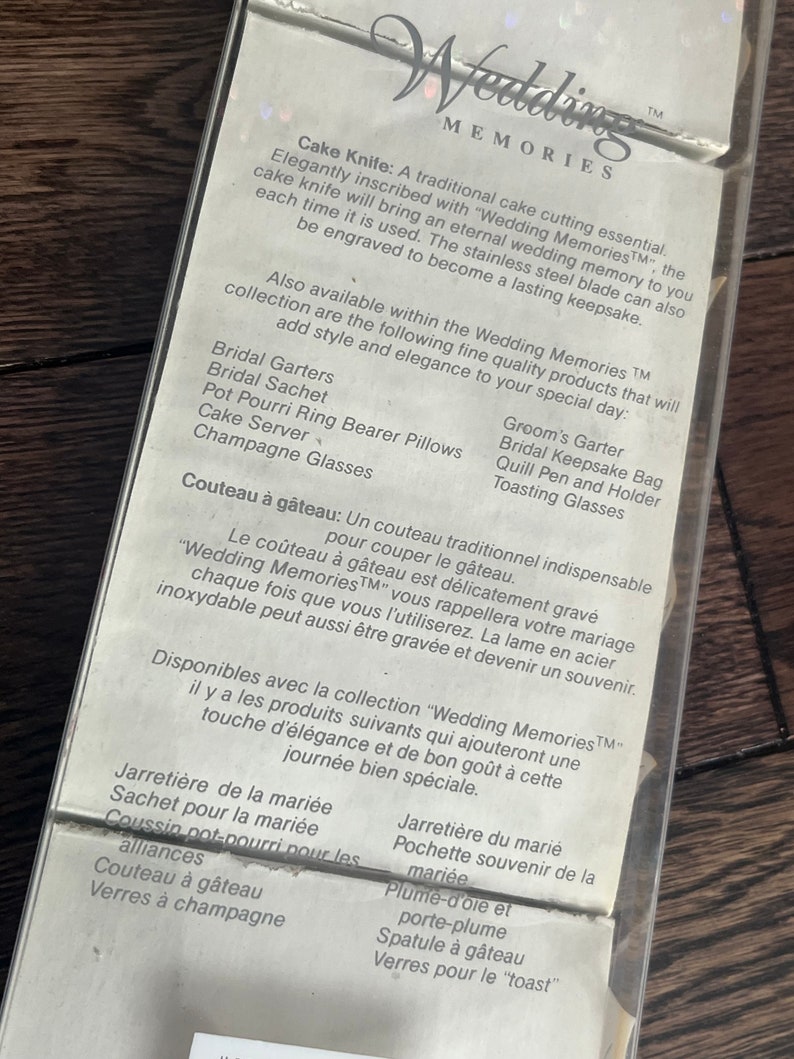 May include: A white card with the text "Wedding Memories" in black lettering. The card lists various wedding-related items, including a cake knife, garters, a keepsake bag, and toasting glasses. The text "Wedding Memories" is a trademark.