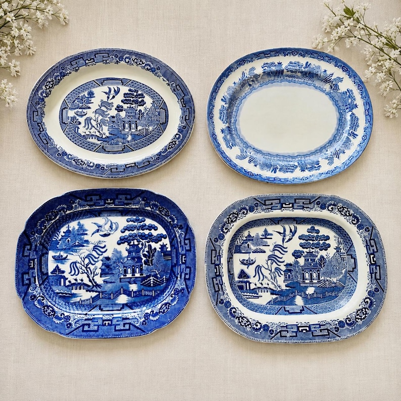 May include: Four oval ceramic platters featuring blue and white willow patterns. Three platters display detailed landscape scenes with pagodas, bridges, and birds, while one platter has a plain white center with a decorative blue floral border.