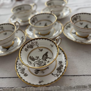 May include: A set of six teacups and saucers with a black and gold floral pattern. The cups and saucers are made of fine china and have a delicate design.