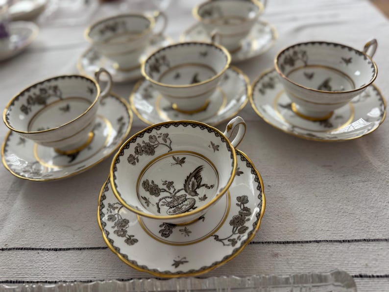 May include: A set of six teacups and saucers with a black and gold floral pattern. The cups and saucers are made of fine china and have a delicate design.