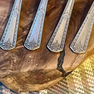 Pu&ograve; includere: Primo piano di quattro forchette color argento con elaborati disegni floreali e a forma di cuore. Le forchette sono disposte su una superficie di legno, mostrando i loro dettagli intricati. Le posate hanno un'estetica classica e vintage.