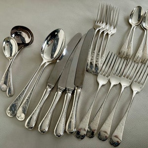 May include: A collection of antique silverware, including spoons, forks, knives, and a ladle. The silverware has a shiny, reflective surface and a floral pattern on the handles. The arrangement suggests a formal dining setting.