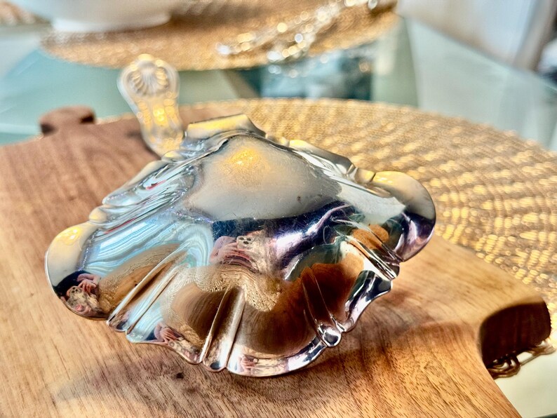 May include: A silver serving spoon with a decorative, scalloped edge. The spoon is made of polished metal and reflects light.