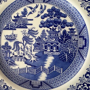 K&ouml;nnte beinhalten: Blaue und wei&szlig;e Keramikplatte mit einem traditionellen Weidenmuster. Das Muster zeigt eine Pagode, eine Br&uuml;cke, einen Weidenbaum und V&ouml;gel.