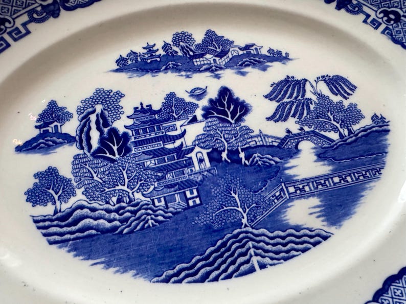 K&ouml;nnte beinhalten: Blau-wei&szlig;e ovale Servierplatte aus Porzellan mit traditionellem chinesischem Landschaftsdesign. Das Design zeigt eine Pagode, B&auml;ume, eine Br&uuml;cke und Wasser.