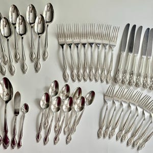 May include: A collection of vintage silverware, including spoons, forks, knives, and butter knives. The silverware is silver-toned with ornate floral detailing on the handles. The spoons have a rounded bowl shape. The forks have four tines.