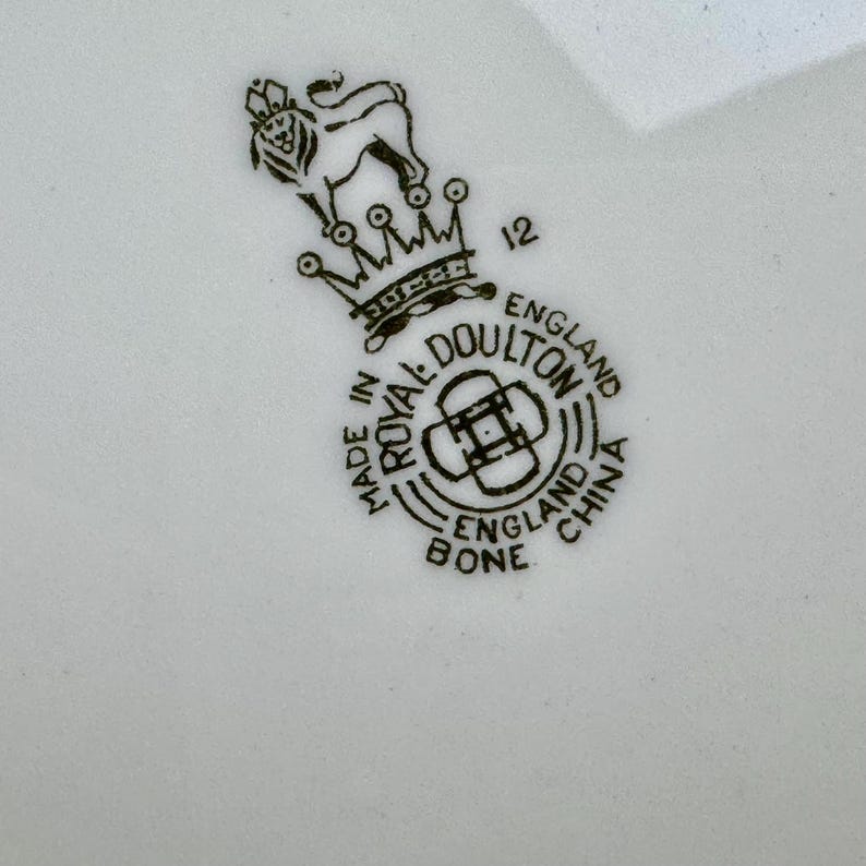 Puede incluir: Sello en blanco y negro con el texto "Made in England Royal Doulton Bone China" y un le&oacute;n con una corona encima. El n&uacute;mero "12" est&aacute; impreso a la derecha de la corona.