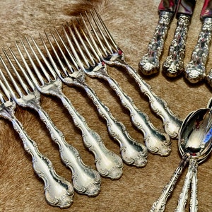 May include: A set of silver flatware, including forks and spoons, with ornate handles. The forks have a decorative design with a scalloped edge. The spoons have a similar design with a rounded bowl.