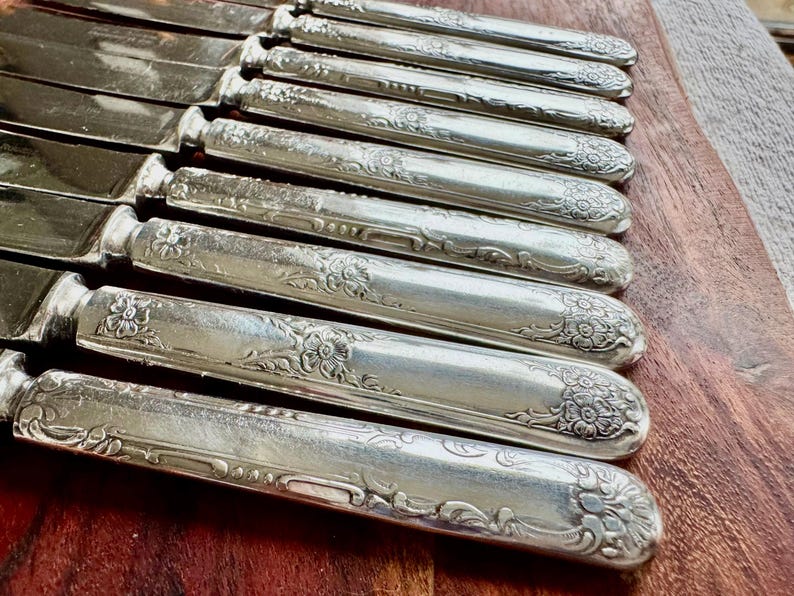 May include: A set of silver-plated dinner knives with ornate floral designs on the handles.