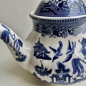 K&ouml;nnte beinhalten: Eine blaue und wei&szlig;e Porzellan-Teekanne mit traditionellem chinesischem Design. Die Teekanne hat einen Deckel und einen Ausguss. Das Design zeigt einen Weidenbaum, V&ouml;gel und eine Pagode.
