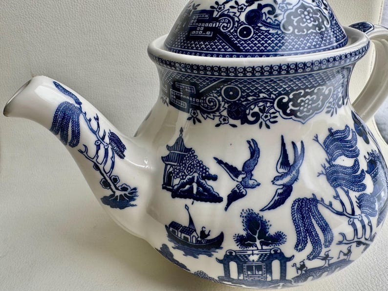 K&ouml;nnte beinhalten: Eine blaue und wei&szlig;e Porzellan-Teekanne mit traditionellem chinesischem Design. Die Teekanne hat einen Deckel und einen Ausguss. Das Design zeigt einen Weidenbaum, V&ouml;gel und eine Pagode.