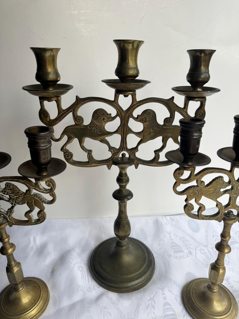 Pu&ograve; includere: Portacandele antichi in ottone con intricati disegni di leoni. Ogni portacandele presenta pi&ugrave; coppe per candele e bracci decorativi. La finitura in ottone anticato conferisce loro un aspetto vintage, perfetto per aggiungere eleganza.