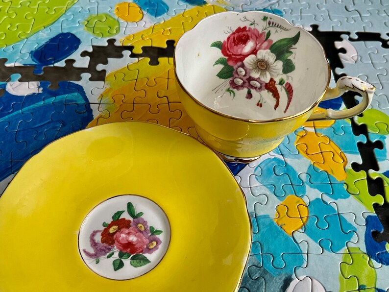 Pu&ograve; includere: Un set composto da tazza e piattino giallo brillante con interno e centro bianchi decorati da un bouquet di fiori colorati. La tazza presenta un bordo smerlato e un manico con finiture dorate, mentre il piattino ha un bordo smerlato abbinato e un motivo floreale centrale.