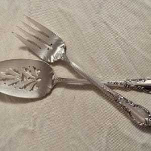 K&ouml;nnte beinhalten: Ein silbernes Kuchenbesteck mit verzierten Griffen. Der Tortenheber hat ein dekoratives, durchbrochenes Design.