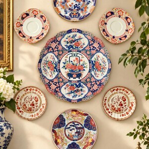 Pu&ograve; includere: Una collezione di sette piatti decorativi in ceramica disposti su una parete. I piatti presentano motivi complessi in blu, rosso, arancione e bianco, inclusi disegni floreali, uccelli ed elementi architettonici con bordi smerlati e circolari.