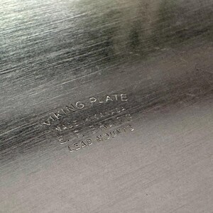 Może przedstawiać: Szczotkowana, srebrzysta powierzchnia metalowa z wygrawerowanym napisem VIKING PLATE, MADE IN CANADA, E.P. BRASS, LEAD MOUNTS. Metaliczna tekstura wykazuje drobne poziome linie ziarna na całym widocznym obszarze przedmiotu.