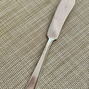 May include: A silver butter knife with a curved blade and a long, slender handle. The knife has a classic design and is made of a shiny, reflective metal. The handle has a decorative end.