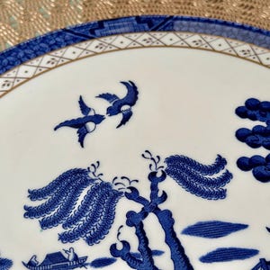 May include: A blue and white porcelain plate with a willow pattern design. The plate features a gold rim and a delicate floral pattern.