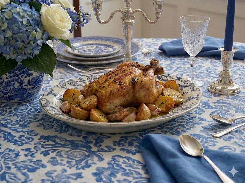 K&ouml;nnte beinhalten: Ein gebratenes H&auml;hnchen und Kartoffeln werden auf einem dekorativen Teller serviert, der auf einem Tisch mit einer blau-wei&szlig;en Blumendecke steht. Auf dem Tisch befinden sich Besteck, ein Kristallweinglas und ein silberner Leuchter. Ein Strau&szlig; blauer Hortensien und wei&szlig;er Rosen befindet sich in einer Vase.
