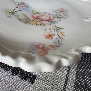 May include: Off-white ceramic serving platter with a scalloped edge. The platter is decorated with a floral design featuring pink and peach flowers, green leaves, and small blue flowers.