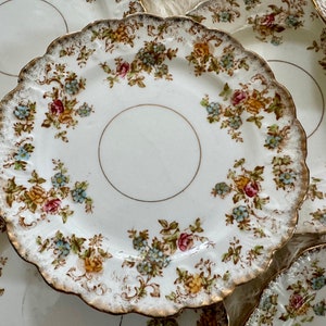 K&ouml;nnte beinhalten: Ein Set vintage Porzellan Teller mit floralem Muster und goldenen Verzierungen. Die Teller haben einen gewellten Rand und ein zartes Blumenmuster in den Farben Rosa, Gelb, Blau und Gr&uuml;n.