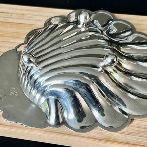 May include: A silver-plated serving dish shaped like a seashell with three feet. The dish has a scalloped edge and a smooth, shiny surface. The bottom of the dish is marked with the text "CRYSTAL  MADE IN  HONG KONG".