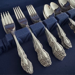 May include: Close-up of a set of ornate silverware, including forks and spoons, arranged in a blue case. The silverware has a detailed floral pattern on the handles and a shiny, reflective surface. The forks and spoons are neatly organized.