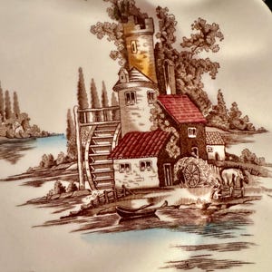 Op de afbeelding: Een wit keramieken bord met een bruine transferware-illustratie van een watermolen met een hoge toren, gebouwen met rode daken, een waterrad, een kleine boot op het water en een paard en wagen bij de rivieroever.