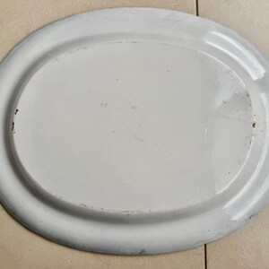 Puede incluir: Una fuente ovalada de esmalte blanco con un borde ligeramente elevado. La fuente tiene una superficie lisa y brillante con algunas imperfecciones menores. El borde es de un tono blanco m&aacute;s claro. Este plato vintage es ideal.