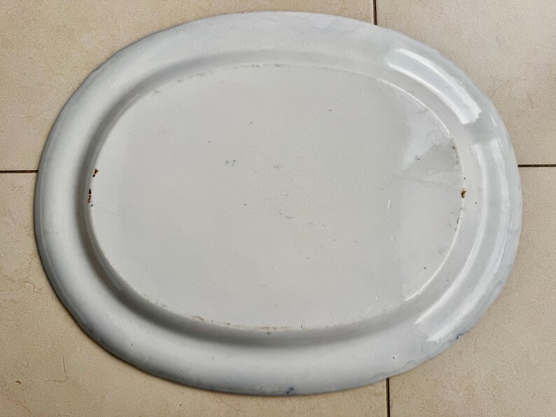 Puede incluir: Una fuente ovalada de esmalte blanco con un borde ligeramente elevado. La fuente tiene una superficie lisa y brillante con algunas imperfecciones menores. El borde es de un tono blanco m&aacute;s claro. Este plato vintage es ideal.