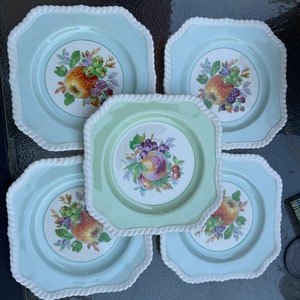 Puede incluir: Juego de cinco platos cuadrados de cer&aacute;mica con fondo azul claro y borde de cuerda blanca. Cada plato presenta un dise&ntilde;o de frutas coloridas en el centro.