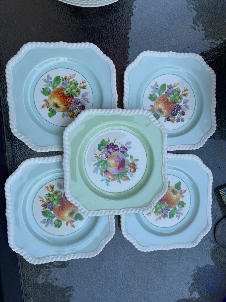 Puede incluir: Juego de cinco platos cuadrados de cer&aacute;mica con fondo azul claro y borde de cuerda blanca. Cada plato presenta un dise&ntilde;o de frutas coloridas en el centro.