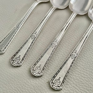 Puede incluir: Cuatro cucharas de plata con diseños ornamentados en los mangos. Las cucharas están dispuestas en fila, con los mangos apuntando hacia la derecha.