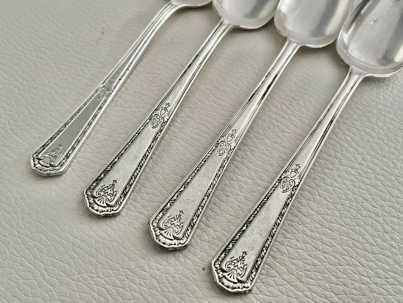 Pu&ograve; includere: Quattro cucchiai d'argento con manici ornati e dettagliati e conche arrotondate. I cucchiai presentano un bordo decorativo lungo il manico e un motivo floreale sulla punta. I cucchiai sono disposti in diagonale.