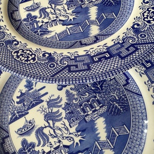 K&ouml;nnte beinhalten: Zwei blaue und wei&szlig;e Keramikteller mit einem traditionellen Weidenmuster. Die Teller sind &uuml;bereinander gestapelt.