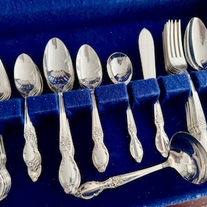 K&ouml;nnte beinhalten: Ein Set silbernes Besteck in einem blauen Samt-Etui. Das Set enth&auml;lt Gabeln, L&ouml;ffel und ein Messer.