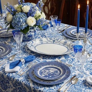 K&ouml;nnte beinhalten: Ein festlich gedeckter Esstisch mit blau-wei&szlig;em Porzellan, Kristallgl&auml;sern und Silberbesteck. Der Tisch ist mit einem Blumengesteck und brennenden Kerzen geschm&uuml;ckt, alles auf einer gemusterten Tischdecke. Eine klassische und elegante Einrichtung.