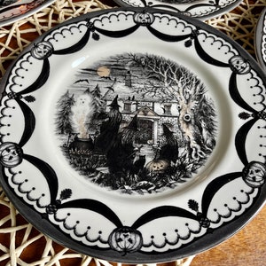 K&ouml;nnte beinhalten: Schwarz-wei&szlig;er Halloween-Dinnerteller mit einem Spukhaus, Hexen und einem Kessel. Der Teller hat einen schwarz-wei&szlig;en gewellten Rand mit K&uuml;rbissen.