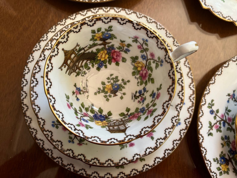 K&ouml;nnte beinhalten: Ein wei&szlig;es Tee-Set mit goldener Verzierung und einem floralen Muster. Das Muster zeigt eine Pagode, Blumen und V&ouml;gel. Die Untertasse hat einen doppelten Rand.