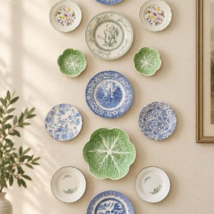 May include: A collection of twelve decorative ceramic plates arranged on a wall. The display includes blue and white transferware, white plates with floral patterns, and green cabbage-shaped plates in various sizes and circular shapes.