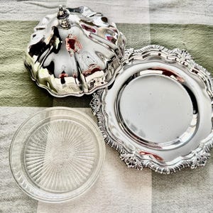 May include: A silver-plated butter dish with a lid, a decorative plate, and a clear glass plate. The butter dish has a fluted design and a small handle on top. The decorative plate has a scalloped edge.