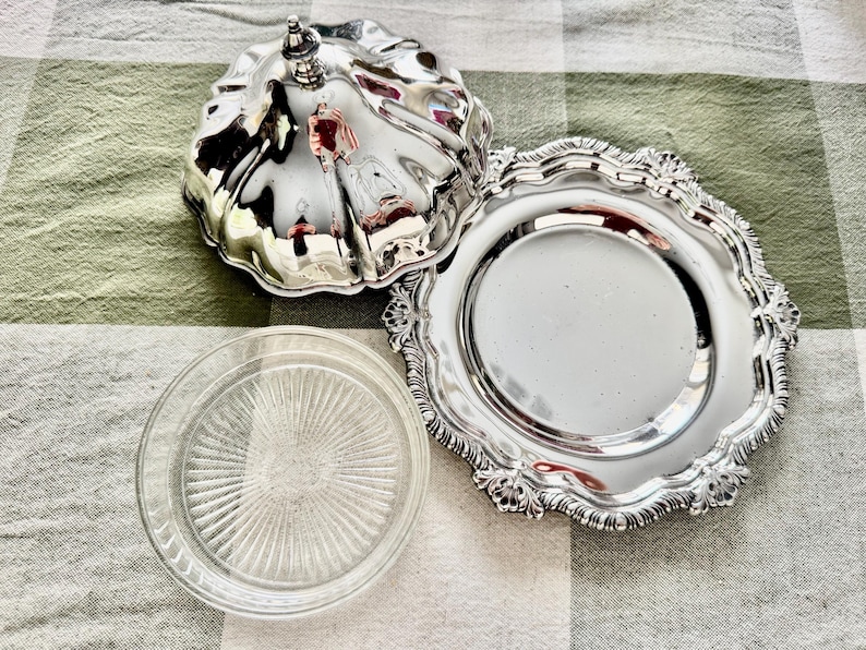 May include: A silver-plated butter dish with a lid, a decorative plate, and a clear glass plate. The butter dish has a fluted design and a small handle on top. The decorative plate has a scalloped edge.