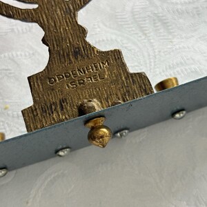 May include: Close-up of a vintage menorah with a brass finish. The base is inscribed with "OPPENHEIM ISRAEL". The menorah has holders for candles and is decorated with small, clear rhinestones.