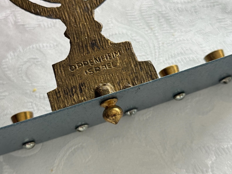 May include: Close-up of a vintage menorah with a brass finish. The base is inscribed with "OPPENHEIM ISRAEL". The menorah has holders for candles and is decorated with small, clear rhinestones.