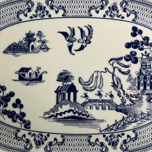 May include: An oval ceramic platter featuring a blue and white willow pattern. The design includes two birds in flight, a small boat with a person, a bridge with three figures, a pagoda, and willow trees, all framed by a decorative lattice border.
