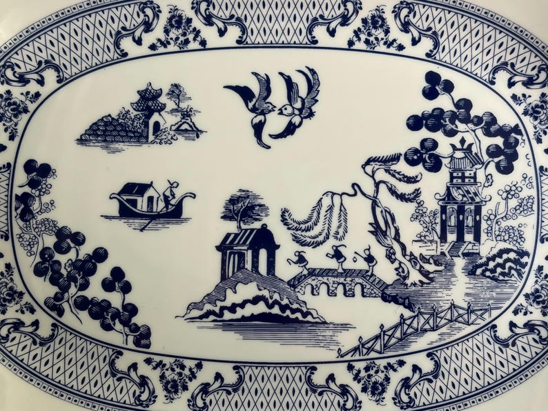 May include: An oval ceramic platter featuring a blue and white willow pattern. The design includes two birds in flight, a small boat with a person, a bridge with three figures, a pagoda, and willow trees, all framed by a decorative lattice border.