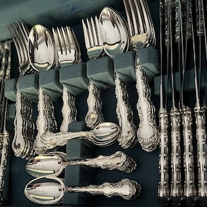May include: A complete set of ornate silver silverware, including forks, knives, and spoons, neatly arranged in a blue storage case. The silverware features detailed floral patterns on the handles, reflecting a classic and elegant design. The set is ideal for formal dining.