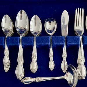 K&ouml;nnte beinhalten: Ein Set aus silbernem Besteck in einem blauen Samt-Etui. Das Set enth&auml;lt Gabeln, L&ouml;ffel und ein Buttermesser.