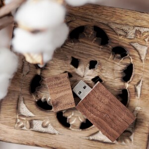Könnte beinhalten: Ein rechteckiger USB-Stick mit einem dunkelbraunen Holzgehäuse und einer passenden abnehmbaren Holzkappe, ausgestattet mit einem silbernen Metallanschluss, liegend auf einer quadratischen Holzschatulle mit geschnitzten Blumenmustern.