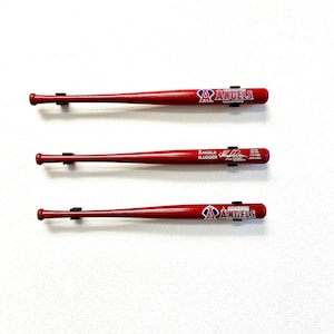 May include: Three red wooden baseball bats with the Anaheim Angels logo and the words "Angels Slugger" on the bats. The bats are mounted on a white wall.